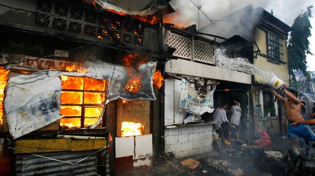 Morador usa um balde de água para apagar um incêndio em uma favela no Tramo, cidade de Pasa, próxima a Manila, capital das Filipinas