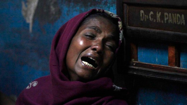 Mulher chora por parente que morreu, ao consumir bebida alcoólica adulterada, em hospital de Porto Diamante, Índia