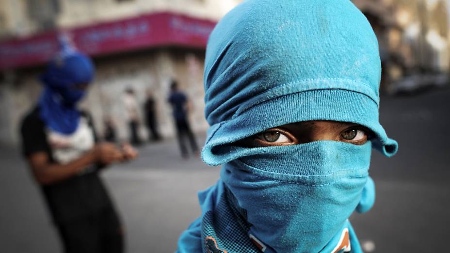 Homem cobre o rosto durante confrontos entre manifestantes e policiais do Bahrein após um protesto contra a realização do GP de Fórmula 1 no país