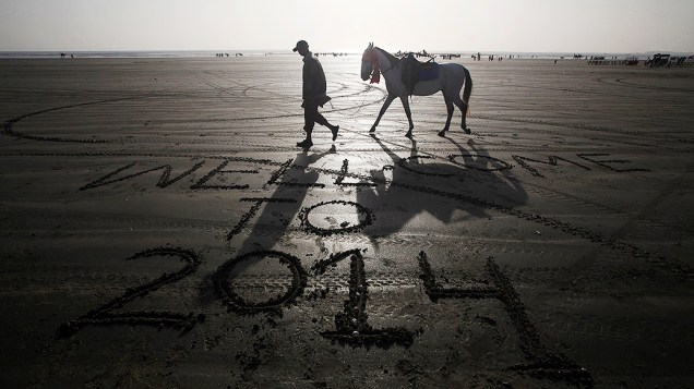 Homem conduz seu cavalo por uma praia com uma mensagem deixada por um visitante na areia na véspera do Ano Novo, em Karachi, Paquistão