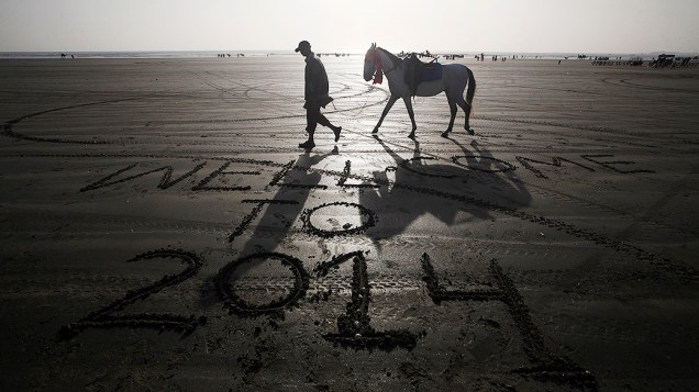 Homem conduz seu cavalo por uma praia com uma mensagem deixada por um visitante na areia na véspera do Ano Novo, em Karachi, Paquistão Homem conduz seu cavalo por uma praia com uma mensagem deixada por um visitante na areia na véspera do Ano Novo, em Karachi, Paquistão