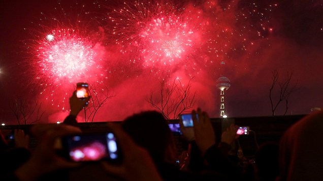 Visitantes tiram fotos e vídeos, do show de fogos de artifício sobre Oriental Pearl Tower, em Xangai, na China