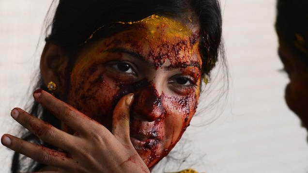 Professora limpa o rosto depois tê-lo manchado com uma pasta vegetal durante as celebrações do Festival Holi, na Índia