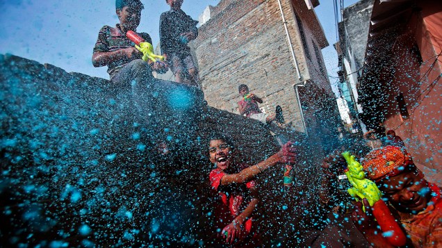 Crianças jogam sprays coloridos durante Festival Holi, em uma pista perto do Templo Bihari Bankeyem, norte do estado de Uttar, Índia