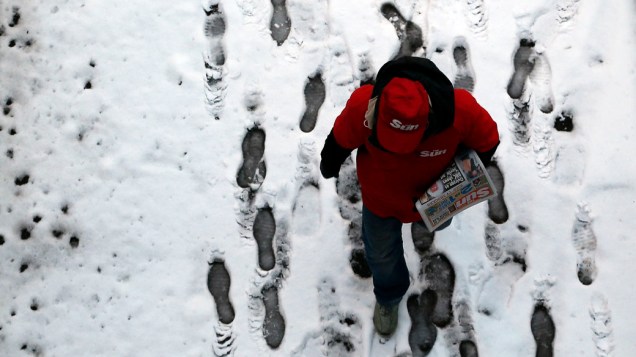 Entregador de jornais caminha em meio a neve em Londres, nesta segunda-feira (21)