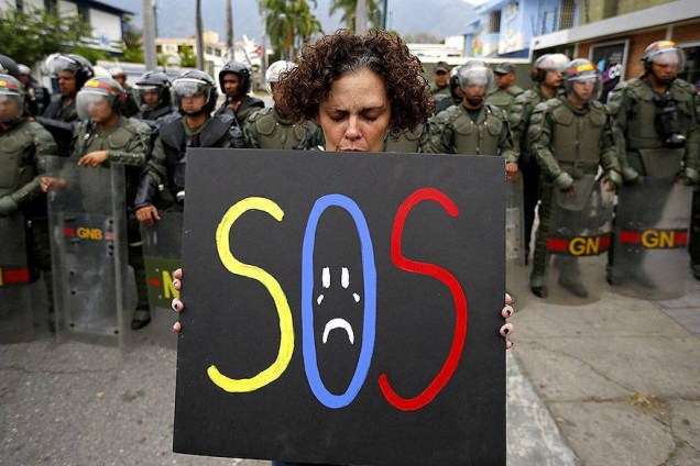 Manifestante segura um cartaz em frente a policiais da guarda nacional em frente a embaixada de Cuba em Caracas, na Venezuela - 25/02/2014