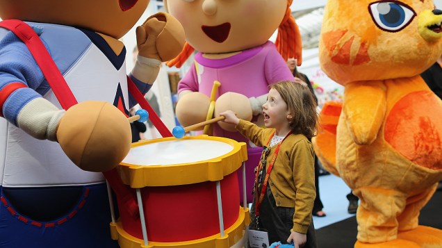 Garota de 4 anos interage com mascotes de desenho animado durante a feira anual de brinquedos de Londres