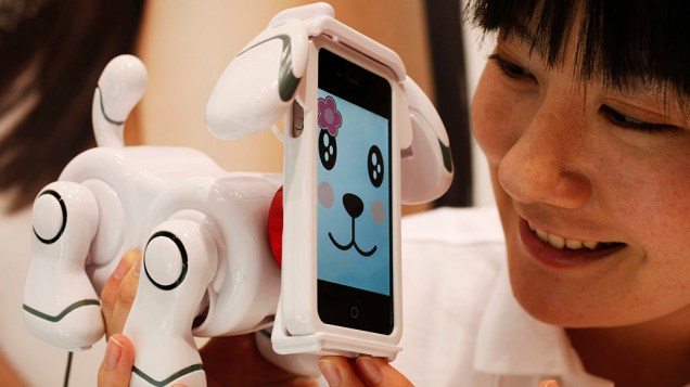 Assistente da fabricante de brinquedos Bandai olha para o "Smart Pet", cão robótico, que tem um iPhone da Apple montado como cara