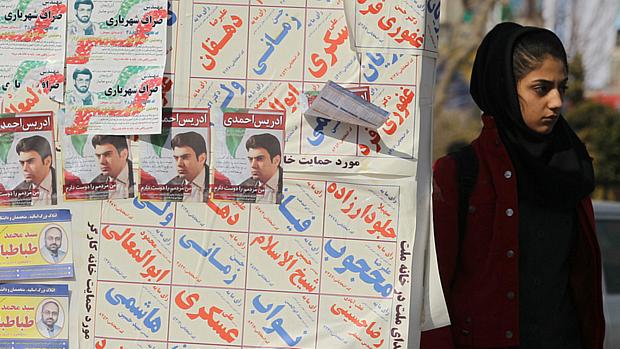 Mulher iraniana ao lado de panfletos das eleições parlamentares de março