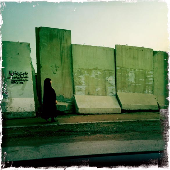 Mulher iraquiana anda em frente à barreiras de concreto, em Bagdá