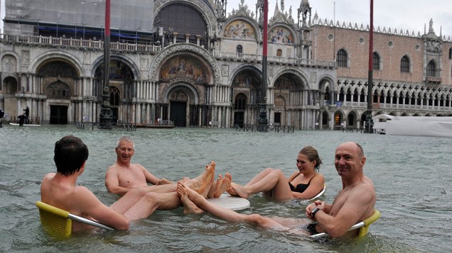 Turistas sentam na praça de São Marcos, durante o período de cheias, em Veneza