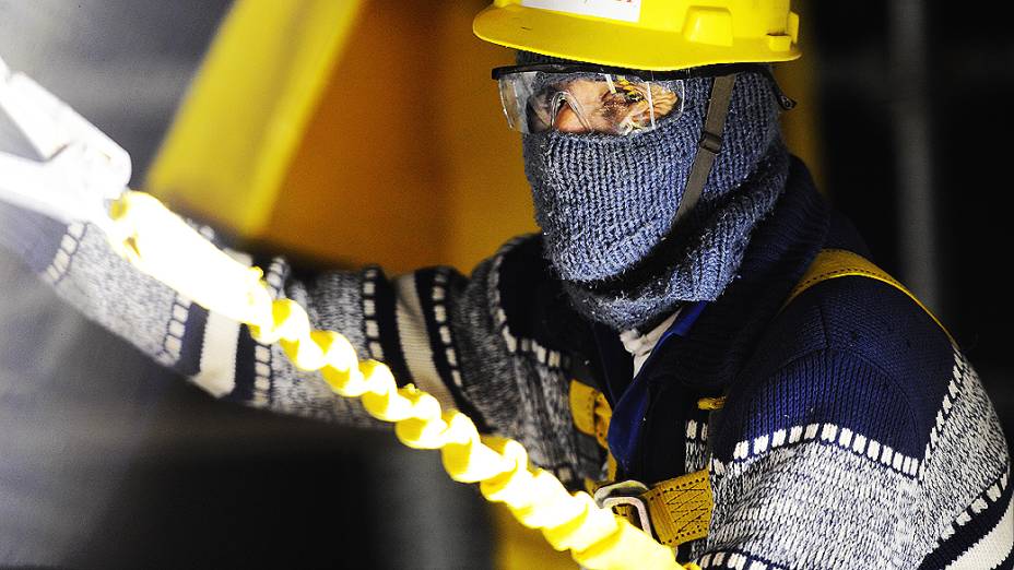 Operário trabalha com uniforme composto por mangas compridas, luvas, botas, capacete e equipamentos de segurança
