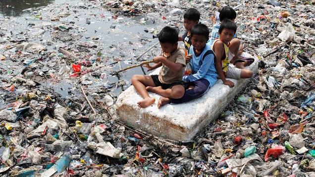 Crianças improvisam bote para flutuar em um rio tomado pelo lixo em Jacarta, na Indonésia