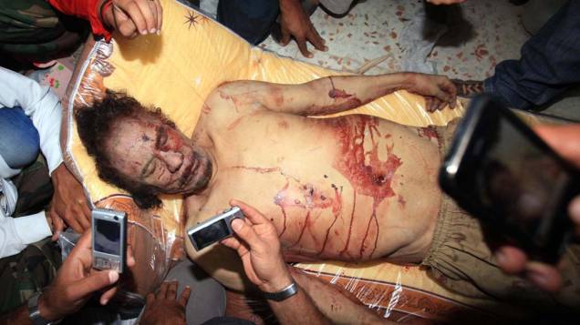 Líbios fotografam o corpo de Muamar Kadafi em Misrata. Após 42 anos à frente do governo da Líbia, Kadafi foi capturado em um buraco que utilizava como esconderijo