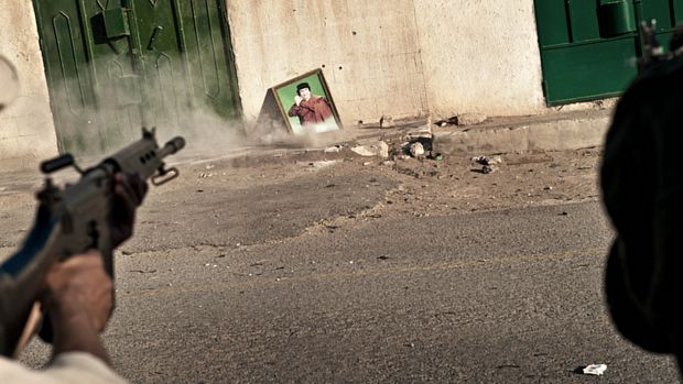Rebelde atira contra quadro com a imagem de Kadafi após a conquista da cidade de Ryayna