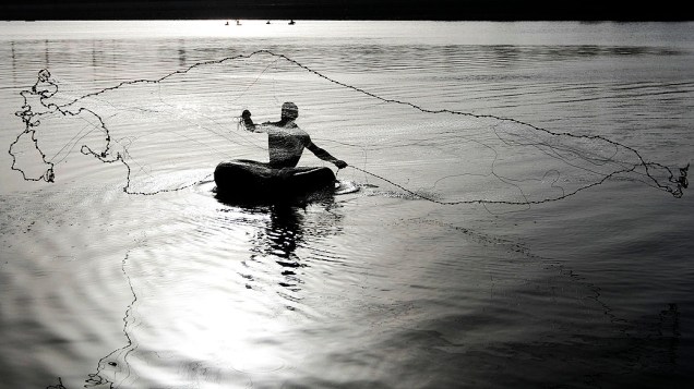 Pescador usa tubos de borracha para flutuar nas águas do rio Sabarmati, em Ahmedabad, na Índia