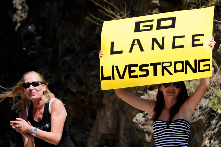 Fã espera Lance Armstrong com a placa "Go Lance Livestrong", uma referência a fundação do ciclista