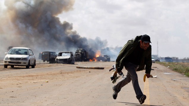 Rebelde líbio corre durante ataque aéreo contra forças de Muamar Kadafi, em estrada que liga Bengasi e Ajdabitah, na Líbia
