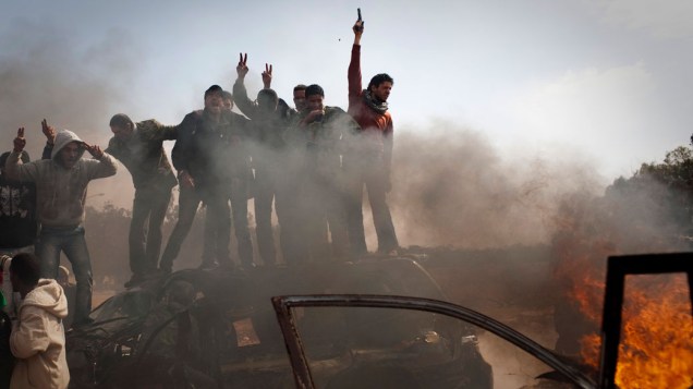 Rebeldes comemoram próximos de carros das forças de Kadafi em chamas, na cidade de Bengasi, na Líbia
