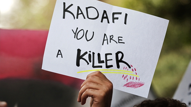 Manifestante levanta cartaz com os dizeres: ‘Kadafi, você é um assassino’