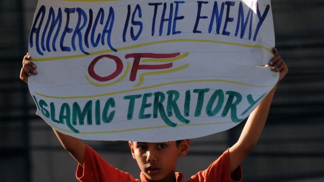 No Paquistão, criança em protesto contra as operações militares na Líbia, mostra cartaz com a frase “A América é inimiga do território islâmico”