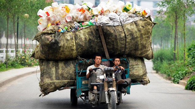 Dois jovens carregam garrafas recicláveis em um triciclo motorizado por uma rua de Taiyuan, na província de Shanxi