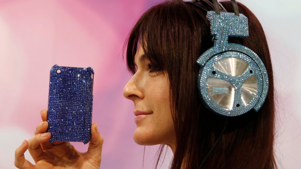 Luxo: Promotora mostra fone de ouvido customizado pela empresa Iwave no valor de 2.000 dólares. Capa para iPhone com cristais Swarovski está à venda por 250 dólares