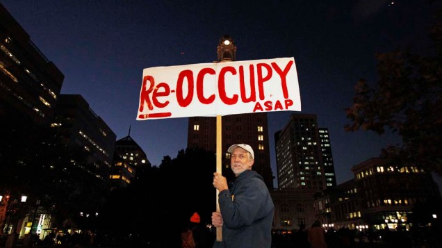 Manifestante do movimento Occupy Wall Street segura placa escrito "Re-Ocupe" em Oakland, Califórnia