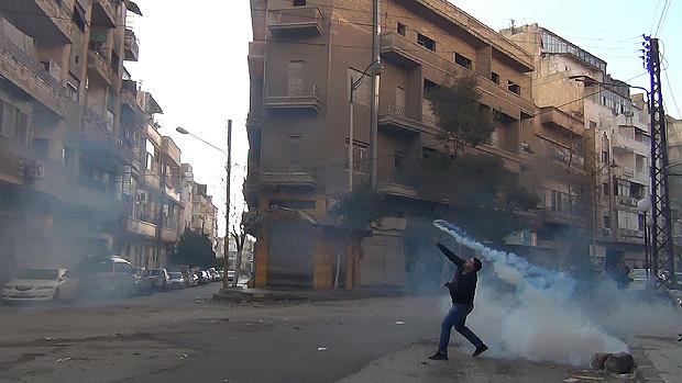 Manifestante lança bomba de gás contra as forças de segurança da Síria em Homs