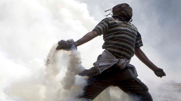 Manifestante arremessa de volta bomba de gás lacrimogênio jogada pela polícia durante confronto em rua próxima a praça Tahrir no Cairo, Egito