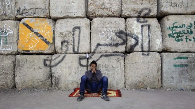 Manifestante senta embaixo de muro com a mensagem "livre" durante protesto contra o governo militar no Cairo, Egito