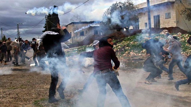 Manifestantes palestinos em meio a latas de gás lacrimogênio atiradas por soldados israelenses durante protesto contra o assentamento judaico de Cadonmen na Cisjordânia