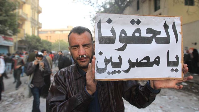 Manifestante mostra placa com os dizeres "Nos ajude povo do Egito" durante o terceiro dia de confrontos na praça Tahrir no Cairo, no Egito
