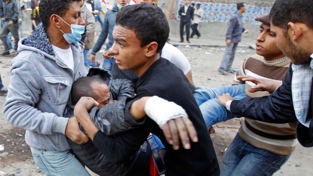 Manifestante ferido em conflito é carregado durante o terceiro dia de confrontos na praça Tahrir no Cairo, no Egito