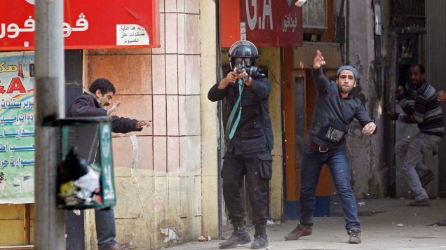 Policial mira arma com balas de borracha em manifestantes que lutam pelo fim do poder militar durante o terceiro dia de confrontos na praça Tahrir no Cairo, no Egito