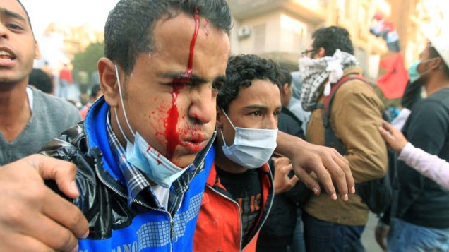 Manifestante ferido em conflito é socorrido durante o terceiro dia de confrontos na praça Tahrir no Cairo, no Egito