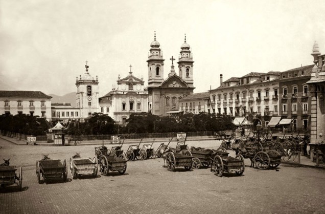 Veículos parados no Largo do Paço, atual Praça Quinze, em meados de 1890. Ao fundo, a antiga fachada da Igreja de Nossa Senhora do Carmo da Antiga Sé.
