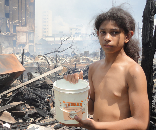 Mateus Izidio, de 10 anos, tenta apagar o que restou do incêndio com as próprias mãos