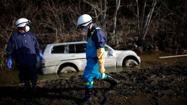 Membros de equipe de resgate procuram corpos em uma área destruída em Ishinomaki, Japão