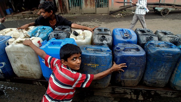 Meninos transportam latas de água em período de monções na cidade de Mumbai, na Índia