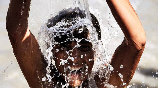 Menino se refresca em uma tubulação de água para escapar do forte calor, no Pakistão