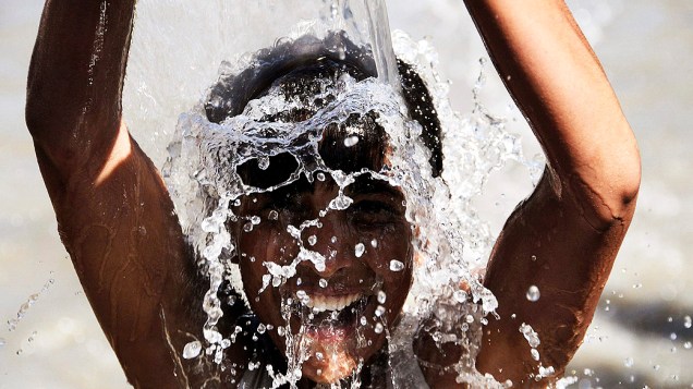 Menino se refresca em uma tubulação de água para escapar do forte calor, no Pakistão