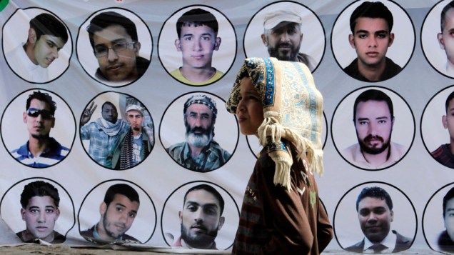 Menino caminha em frente a um painel com fotos de rebeldes mortos durante os conflitos na Líbia