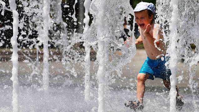 Criança corre no meio da fonte no centro de Donetski, da Ucrânia; temperaturas chegaram até 35 graus