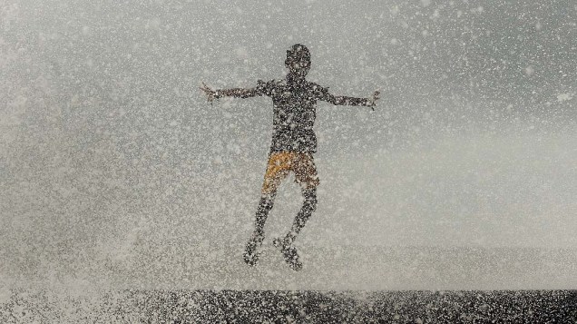 Menino indiano brinca numa onda depois de pancadas de chuva em Mumbai