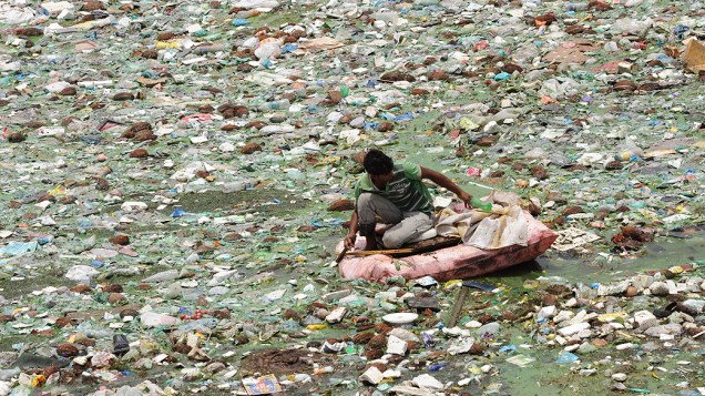 Indiano flutua em uma embarcação improvisada busca por objetos reutilizáveis no poluído rio Sabarmati em Ahmedabad