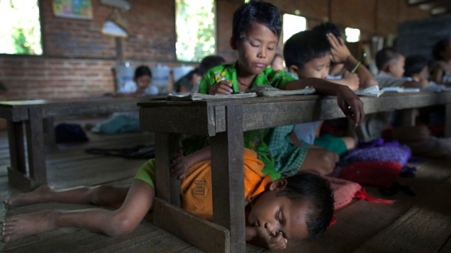 Criança dormindo embaixo da carteira em uma pequena escola pública da cidade de Waw, Mianmar