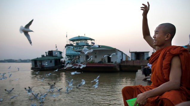 Monje alimenta gaivotas na margem do rio Yangon, Mianmar
