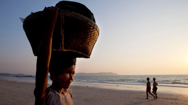Vendedora carrega cesta de mercadorias enquanto turistas passeiam na praia de Ngapali, Mianmar