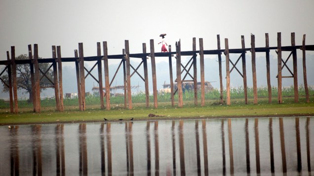 Vendedor cruzando a famosa ponte de U’Bein sobre o lago Taungthaman fora da cidade de Mandalay ao norte de Mianmar
